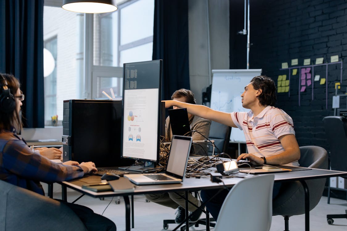 Startup developers collaborating at monitors in a dark-walled office — representing the SOC 2 journey for early-stage SaaS teams.